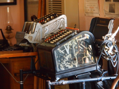 [Two adding machines of which one has a clear side panel showing all the mechanics inside.]